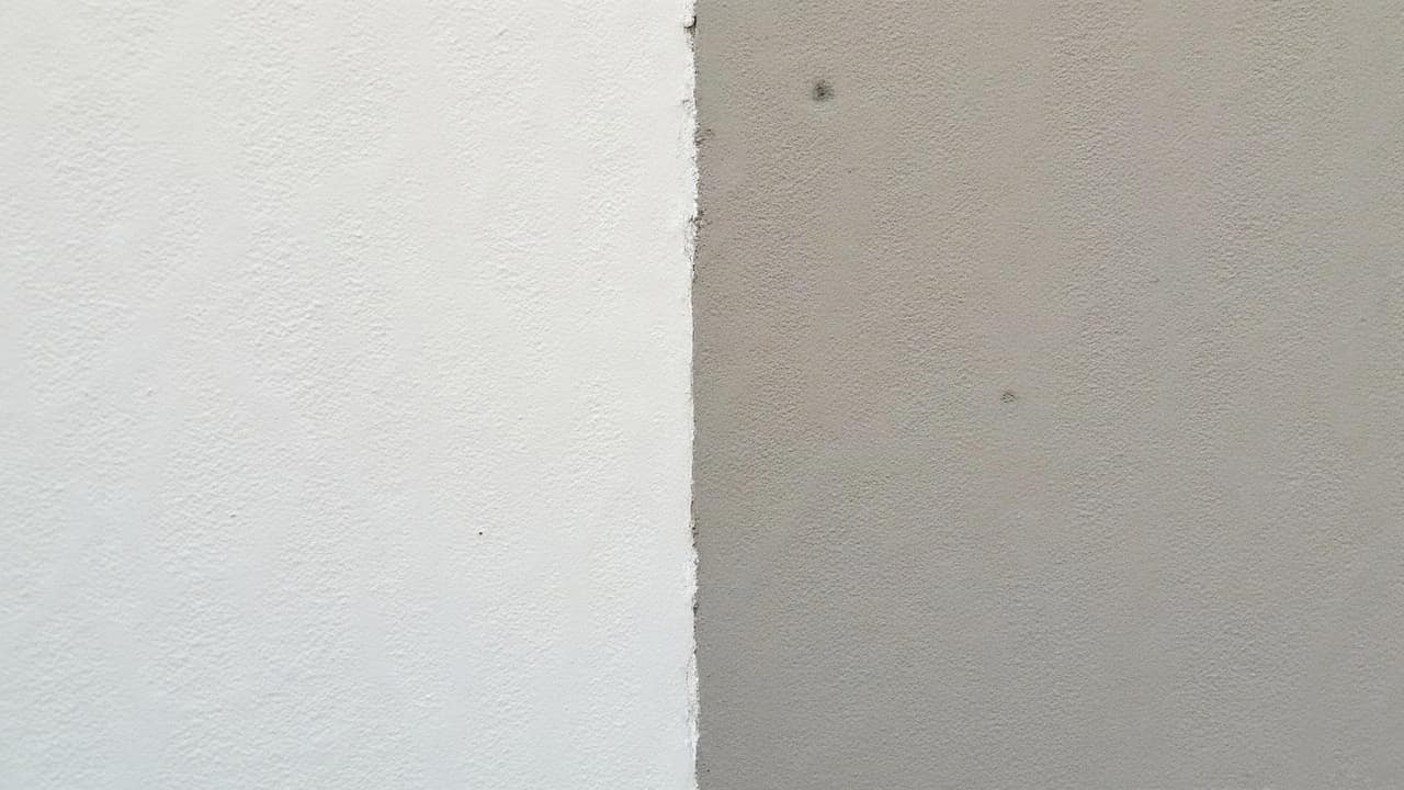 Deux échantillons d'enduit côte à côte sur un mur, l'un fini taloché et l'autre gratté, à proximité d'une zone de brique apparente